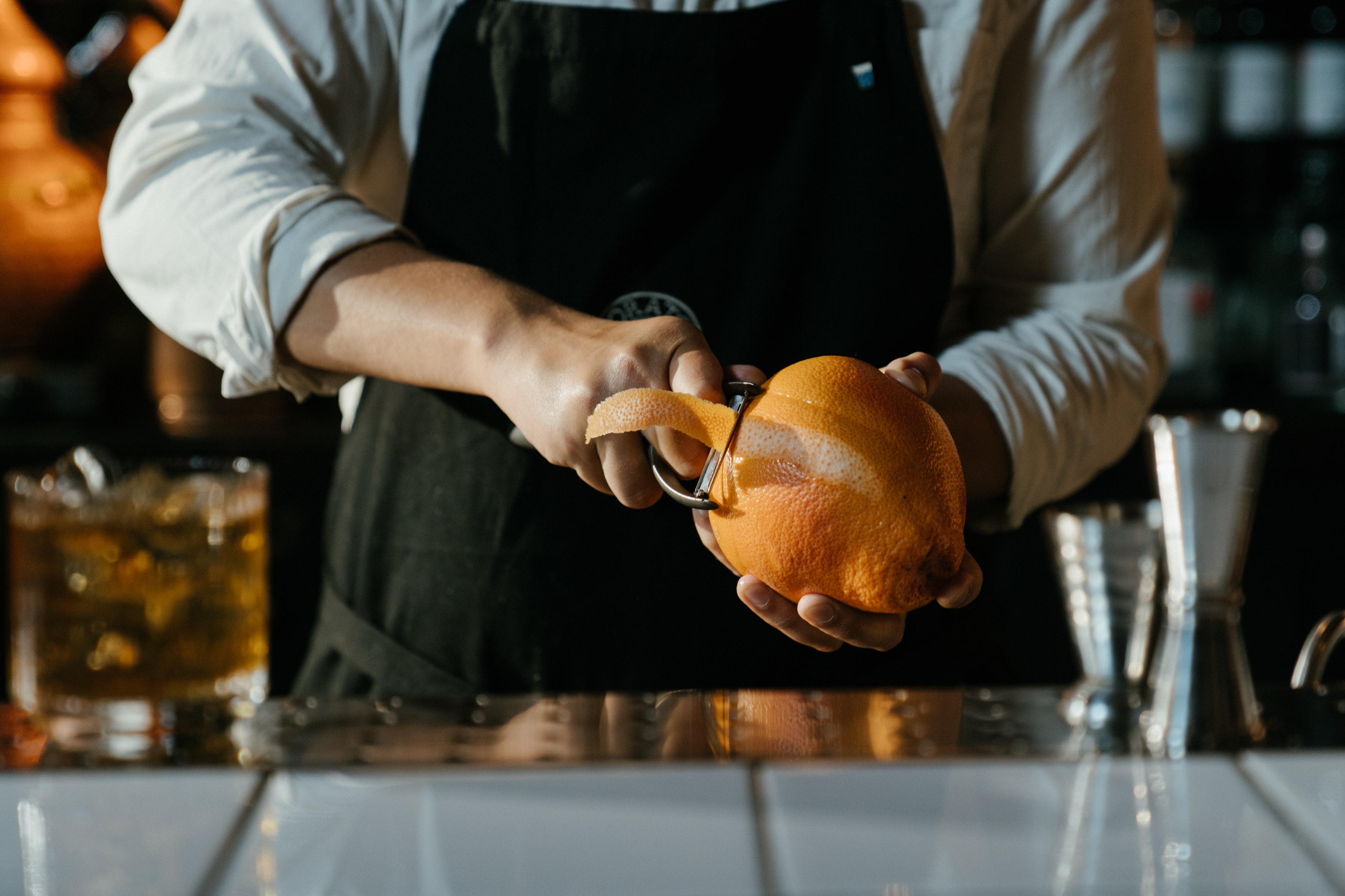 A bartender using a peeler to peel an orange.