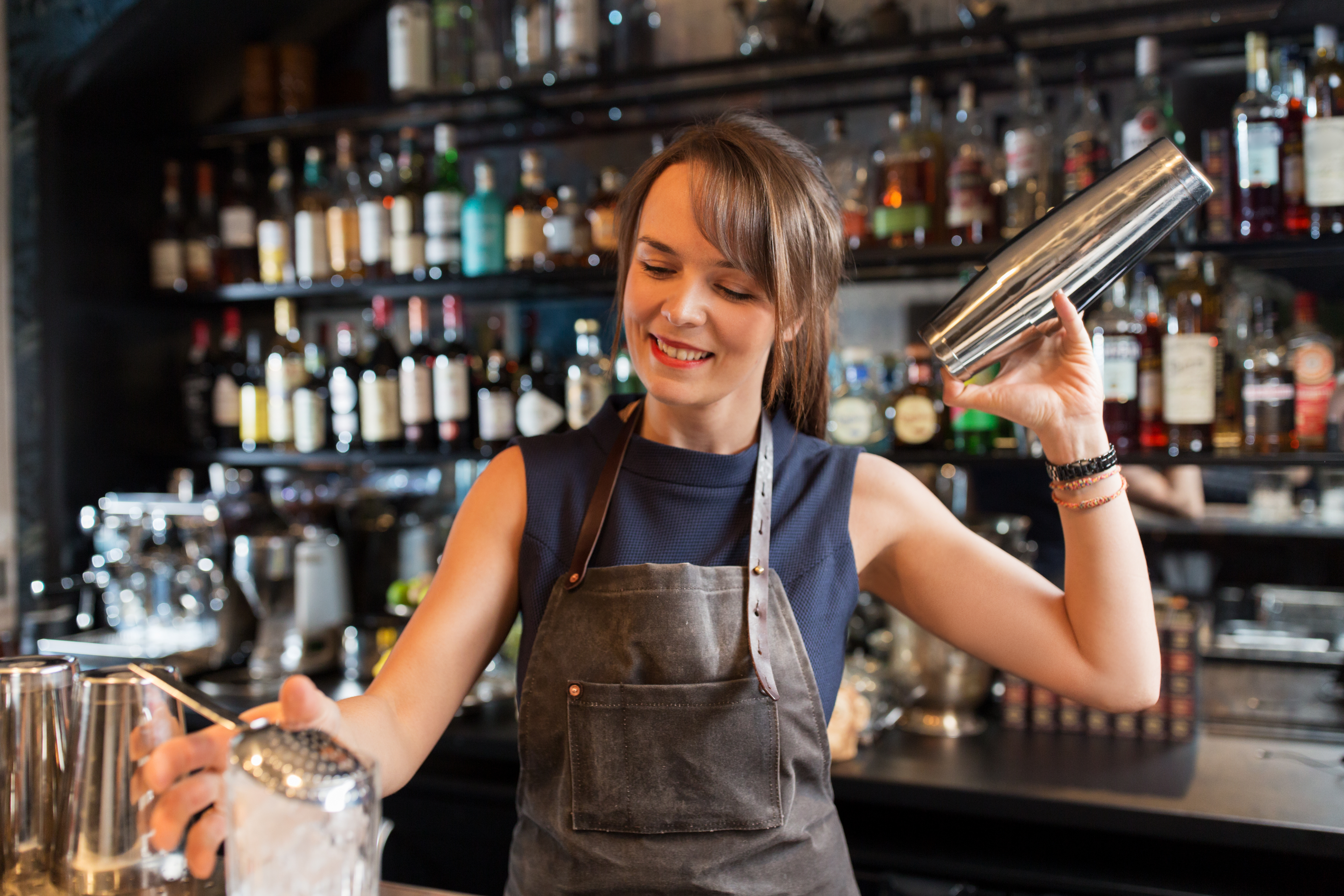 A woman bartender shaking a cocktail behind the bar.