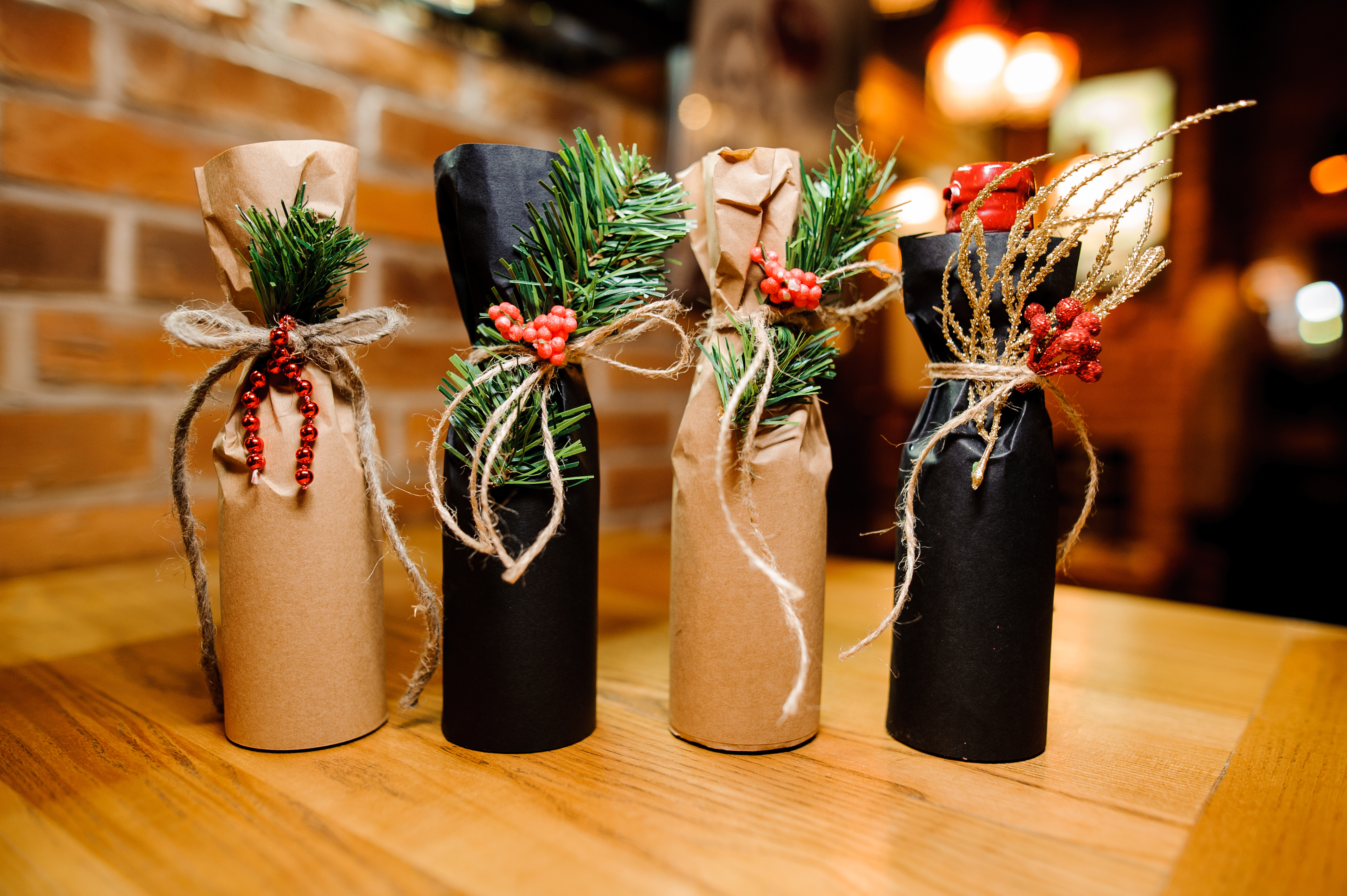 Four bottles wrapped in paper and tied with string and have festive embellishments on it. 