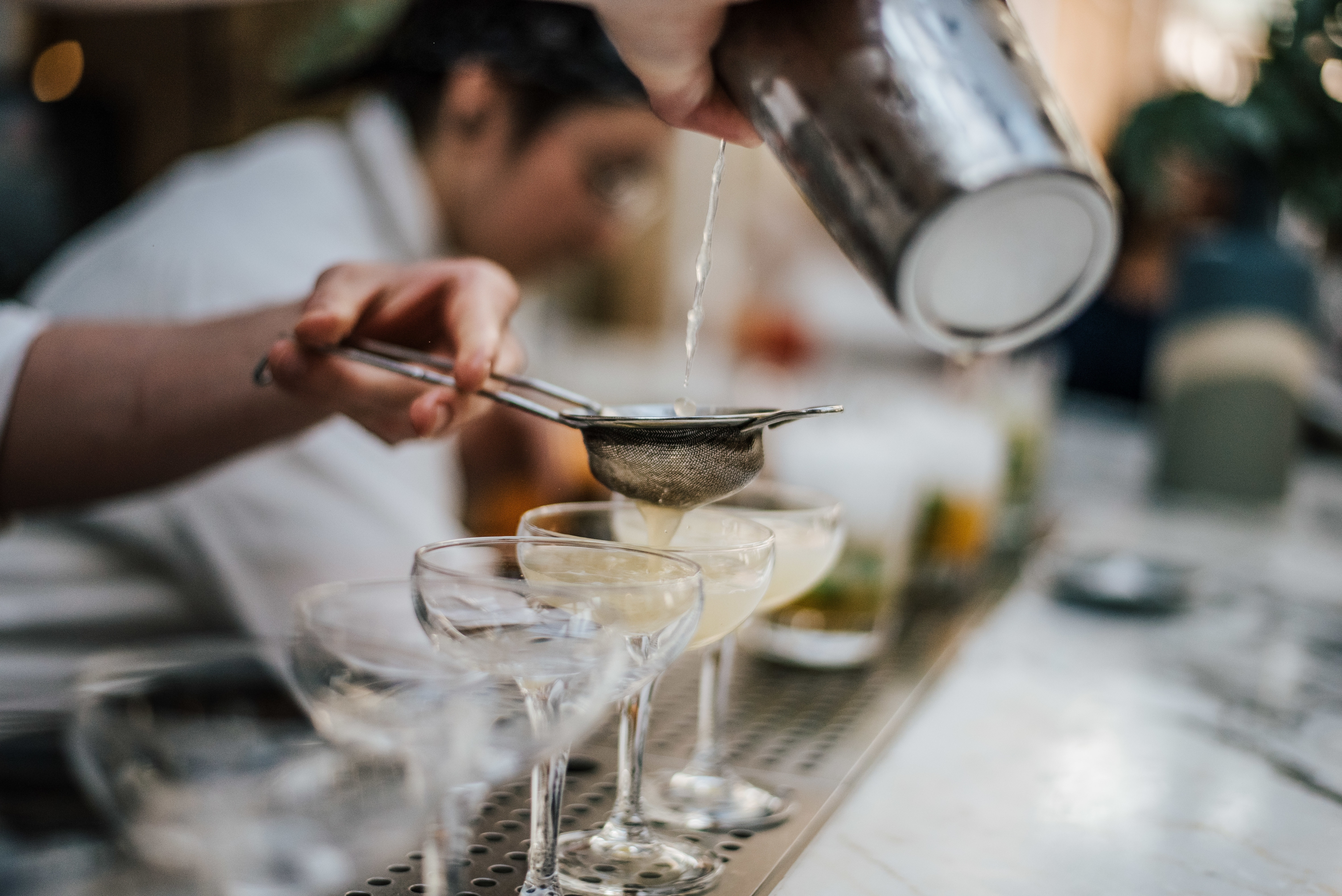 Bartender pouring cocktails into coupe glasses