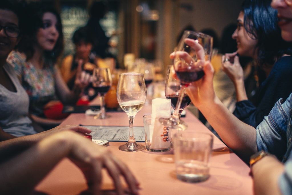 Patrons seated at a restaurant table drinking wine